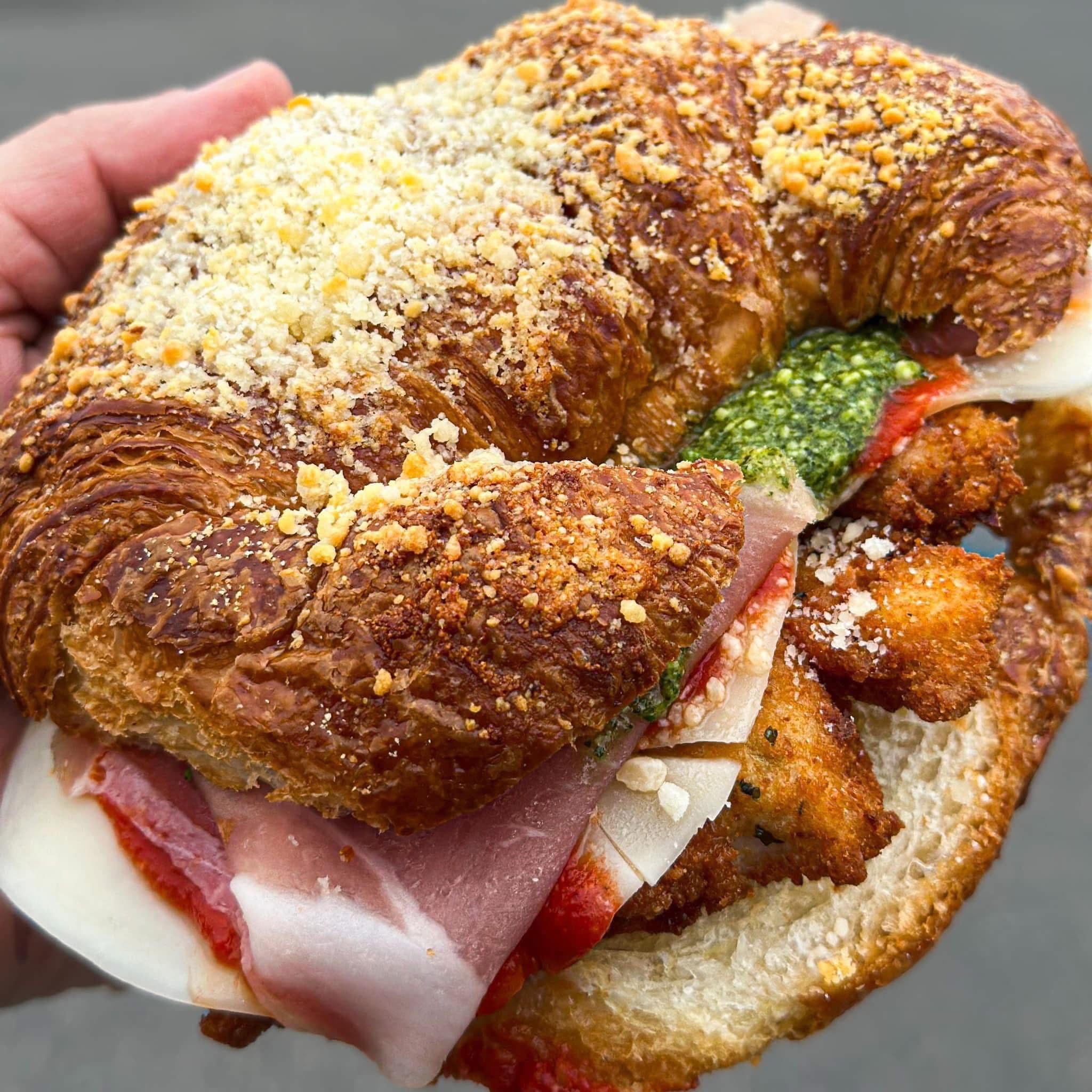 Stuffed Italian deli croissant sandwich with sliced meat, tomato, cheese, and herbs